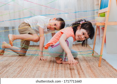 little girl boy brother, siblings, friendschild climbs through a rope web, a game obstacle quest indoors. The concept of active play in the home room, quarantine, self-isolation. - Shutterstock ID 1717711660