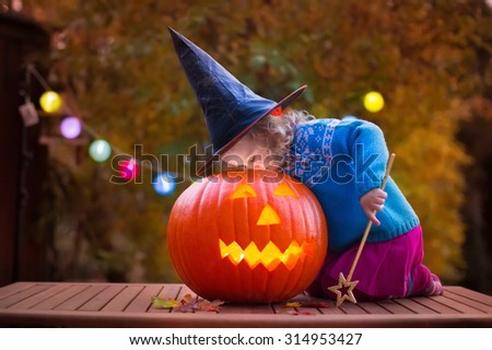 Little girl and boy carving pumpkin at Halloween. Dressed up children trick or treating. Kids trick or treat. Child in witch costume playing in autumn park. Toddler kid with jack-o-lantern. 