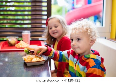 Little Girl And Boy Eating Chicken Nuggets, Hamburger And French Fries In A Fast Food Restaurant. Child With Sandwich And Potato Chips. Kids Eat Unhealthy Fat Food. Fastfood Sandwich For Children.