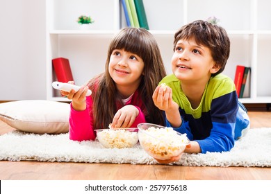 Little Girl And Little Boy Enjoy Eating Popcorn And Watching Tv At Home.Leisure Time For Children