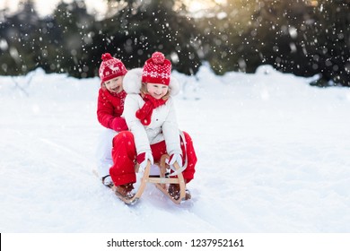 Little Girl And Boy Enjoy A Sleigh Ride. Child Sledding. Toddler Kid Riding A Sledge. Children Play Outdoors In Snow. Kids Sled In Alps Mountains In Winter. Outdoor Fun For Family Christmas Vacation.