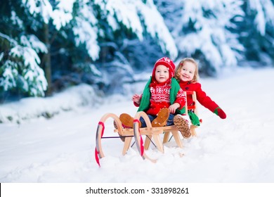 Little Girl And Boy Enjoy A Sleigh Ride. Child Sledding. Toddler Kid Riding A Sledge. Children Play Outdoors In Snow. Kids Sled In Alps Mountains In Winter. Outdoor Fun For Family Christmas Vacation.