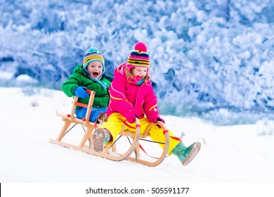 Little Girl And Boy Enjoy A Sleigh Ride. Child Sledding. Toddler Kid Riding A Sledge. Children Play Outdoors In Snow. Kids Sled In Alps Mountains In Winter. Outdoor Fun For Family Christmas Vacation.