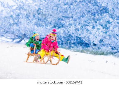 Little Girl And Boy Enjoy A Sleigh Ride. Child Sledding. Toddler Kid Riding A Sledge. Children Play Outdoors In Snow. Kids Sled In Alps Mountains In Winter. Outdoor Fun For Family Christmas Vacation.