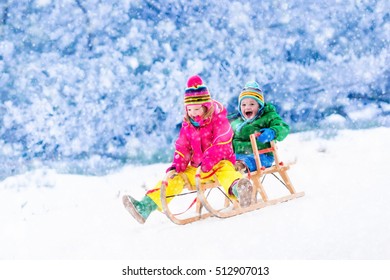 Little Girl And Boy Enjoy A Sleigh Ride. Child Sledding. Toddler Kid Riding A Sledge. Children Play Outdoors In Snow. Kids Sled In Alps Mountains In Winter. Outdoor Fun For Family Christmas Vacation.