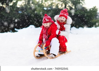 Little Girl And Boy Enjoy A Sleigh Ride. Child Sledding. Toddler Kid Riding A Sledge. Children Play Outdoors In Snow. Kids Sled In Alps Mountains In Winter. Outdoor Fun For Family Christmas Vacation.