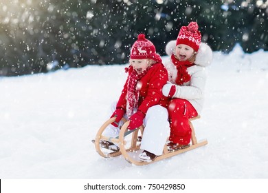 Little Girl And Boy Enjoy A Sleigh Ride. Child Sledding. Toddler Kid Riding A Sledge. Children Play Outdoors In Snow. Kids Sled In Alps Mountains In Winter. Outdoor Fun For Family Christmas Vacation.