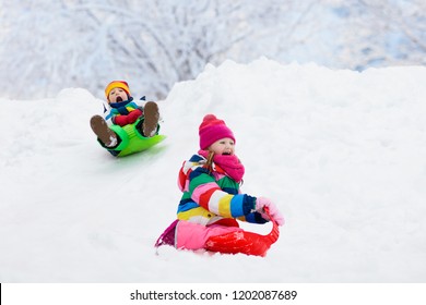 Little Girl And Boy Enjoying Sleigh Ride. Child Sledding. Toddler Kid Riding A Sledge. Children Play Outdoors In Snow. Kids Sled In Snowy Park In Winter. Outdoor Fun For Family Christmas Vacation.