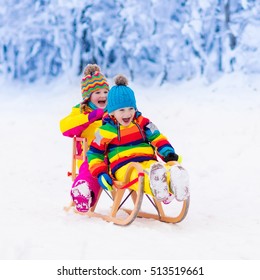 Little Girl And Boy Enjoying Sleigh Ride. Child Sledding. Toddler Kid Riding A Sledge. Children Play Outdoors In Snow. Kids Sled In Snowy Park In Winter. Outdoor Fun For Family Christmas Vacation.