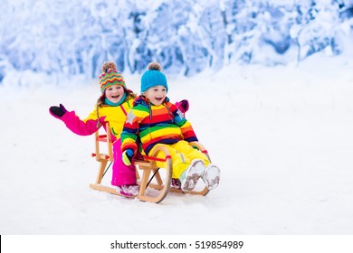 Little Girl And Boy Enjoying Sleigh Ride. Child Sledding. Toddler Kid Riding A Sledge. Children Play Outdoors In Snow. Kids Sled In Snowy Park In Winter. Outdoor Fun For Family Christmas Vacation.