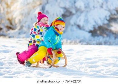 Little Girl And Boy Enjoying Sleigh Ride. Child Sledding. Toddler Kid Riding A Sledge. Children Play Outdoors In Snow. Kids Sled In Snowy Park In Winter. Outdoor Fun For Family Christmas Vacation.