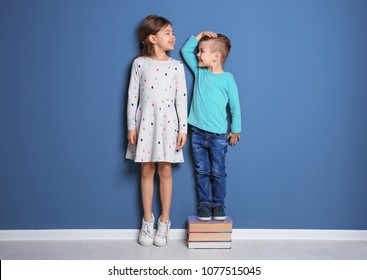 Little girl and boy measuring their height near color wall - Shutterstock ID 1077515045