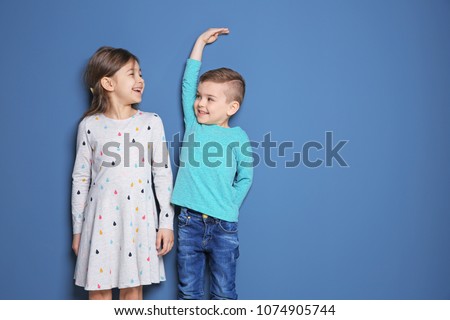 Little girl and boy measuring their height on color background