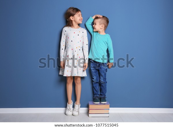 Little girl and boy measuring their height near color wall