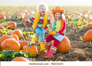 Little Girl And Boy Picking Pumpkins On Halloween Pumpkin Patch. Children Playing In Field Of Squash. Kids Pick Ripe Vegetables On A Farm In Thanksgiving Holiday Season. Family Having Fun In Autumn.