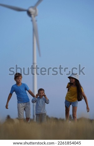 Little girl and boy are running in front of windmills. Renewable energies and sustainable resources wind mills. Children playing with the wind near wind turbine. Sustainable climate visuals