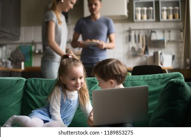 Little Girl And Boy, Son And Daughter Using Laptop, Looking At Screen, Watching Cartoons, Playing Video Game While Parents Cooking, Setting Table, Preparing For Dinner, Family Spending Time Together