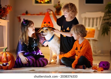 Little Girl And Boy In Witch Costume On Halloween Trick Or Treat. Kids Play With Dog. Candy In Pumpkin Lantern Bucket. Children Celebrate Halloween At Decorated Fireplace. Family Trick Or Treating.