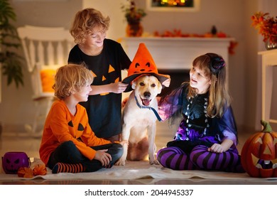 Little Girl And Boy In Witch Costume On Halloween Trick Or Treat. Kids Play With Dog. Candy In Pumpkin Lantern Bucket. Children Celebrate Halloween At Decorated Fireplace. Family Trick Or Treating.