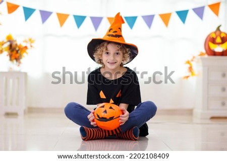 Little girl and boy in witch costume on Halloween trick or treat. Kids holding candy in pumpkin lantern bucket. Children celebrate Halloween at decorated fireplace. Family trick or treating.