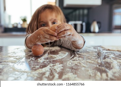 Little Girl Breaking An Egg On Kitchen Counter Covered With Flour. Girl Child Learning Cooking In The Kitchen At Home And Making A Mess.