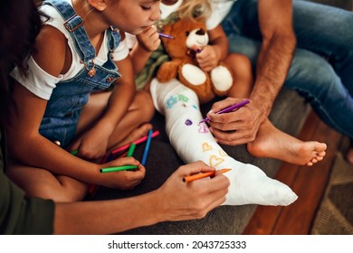 Little girl and broken leg the couch  Mom  dad   two daughters draw plaster and felt  tip pens  The whole family is having fun at home 