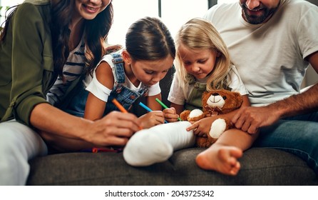 Little girl and broken leg the couch  Mom  dad   two daughters draw plaster and felt  tip pens  The whole family is having fun at home 