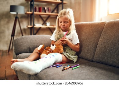 Little Girl With A Broken Leg On The Couch. The Child Draws With Felt-tip Pens On A Plaster Bandage.