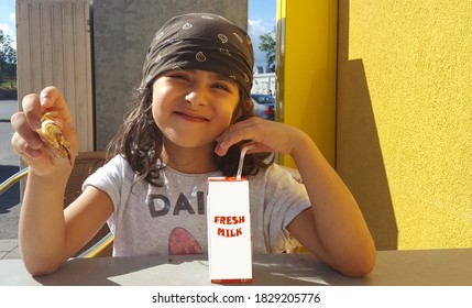 Little Girl With Brown Hair Band Eating Cookies And Drinking Milk Outside In A Sunny Summer Day