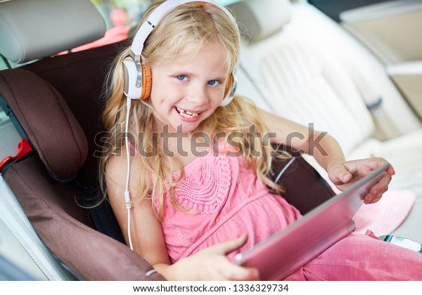 Little girl in the car with headphone and tablet.\
Computer listens to\
music