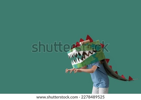 Little girl in cardboard dinosaur costume on green background