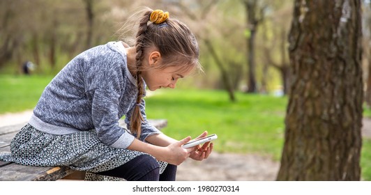 A Little Girl Checks Her Phone, Not Paying Attention To The Beautiful Nature Around.