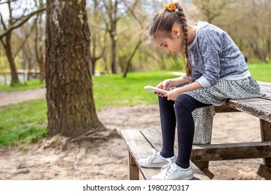 A Little Girl Checks Her Phone, Not Paying Attention To The Beautiful Nature Around.