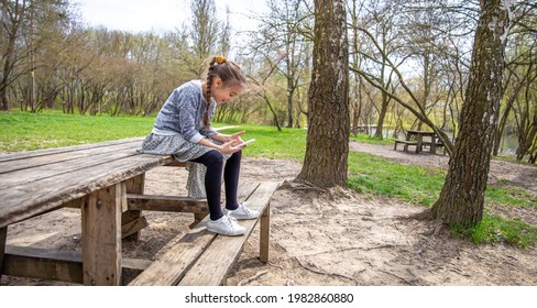 A Little Girl Checks Her Phone, Not Paying Attention To The Beautiful Nature Around.