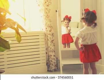 Little Girl Child Fashionista Looking In The Mirror At Home In A Red Skirt, Shoes Of Mother