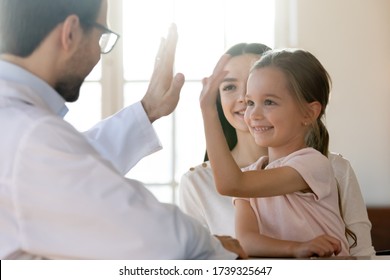 Little Girl Child Give High Five To Positive Male Doctor Or GP At Consultation With Mom, Small Kid Make Deal Celebrate Good Medical Checkup Or Greeting With Smiling Pediatrician At Meeting In Hospital