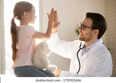 Little girl child give high five greeting with positive male doctor or GP at consultation in clinic, small kid make deal celebrate good medical checkup with smiling pediatrician at meeting in hospital