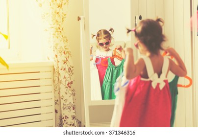 Little Girl Child Looks Into The Mirror And Choose Dresses