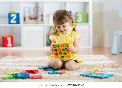 Little girl child playing with lots of colorful plastic digits or numbers on floor indoors.