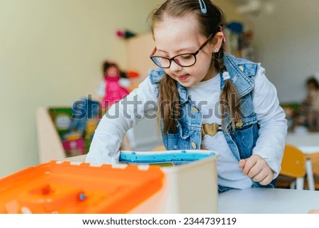 little girl child plays with a children's designer at classroom during break. Developmental activities with children. People with disability.