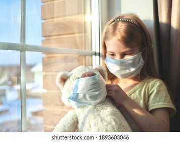 Little Girl Child In Protective Medical Mask Putting Mask On A Bear. Teddy Bear With Protective Mask. The Concept Of Pediatric Healthcare. Stay At Home-quarantine Prevention Of The Coronavirus