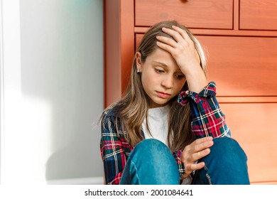 A Little Girl Child Sits Sadly With Her Legs Tucked Up On The Floor. Mental Health, The Concept Of Adolescent Depression