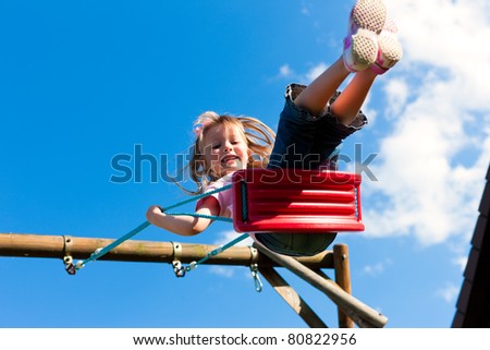 Little girl child sitting on a swing in the garden playground; she has lots of fun