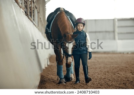 Little girl, child in special uniform and helmet walking with horse during educational course of horseback riding. Animal behavior and care. Sport, childhood, school, active lifestyle, hobby concept