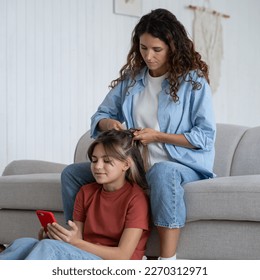 Little girl child using smartphone playing mobile game or surfing internet while mother braiding her hair before school in morning, mom making hairstyle for beloved daughter. Childcare and parenting - Powered by Shutterstock