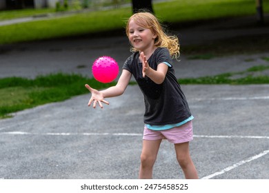 little girl clapped excitedly each time she managed to clear the pink ball over the net. A young girl with blonde hair is playing with a pink ball on a paved playground court. - Powered by Shutterstock