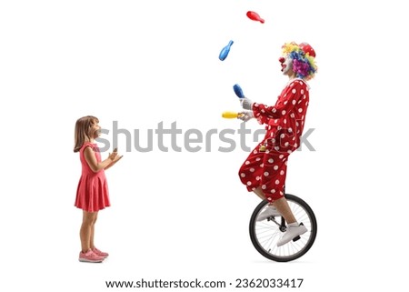 Little girl clapping and watching a clown riding a unicycle and juggling isolated on white background