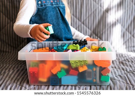 Little girl cleaning up the toy box at home. Child's space organization.