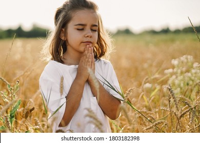 Little Girl closed her eyes, praying in a field wheat. Hands folded in prayer. Religion concept - Shutterstock ID 1803182398