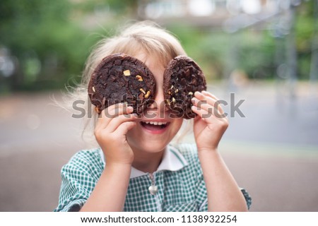 The little girl closing eyes with two big chocolate cookies.